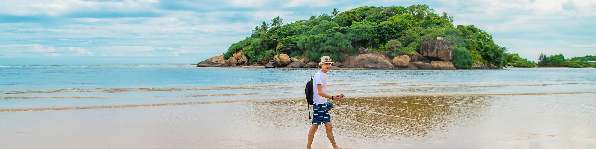 A person walking on a beach with a small island in the background.