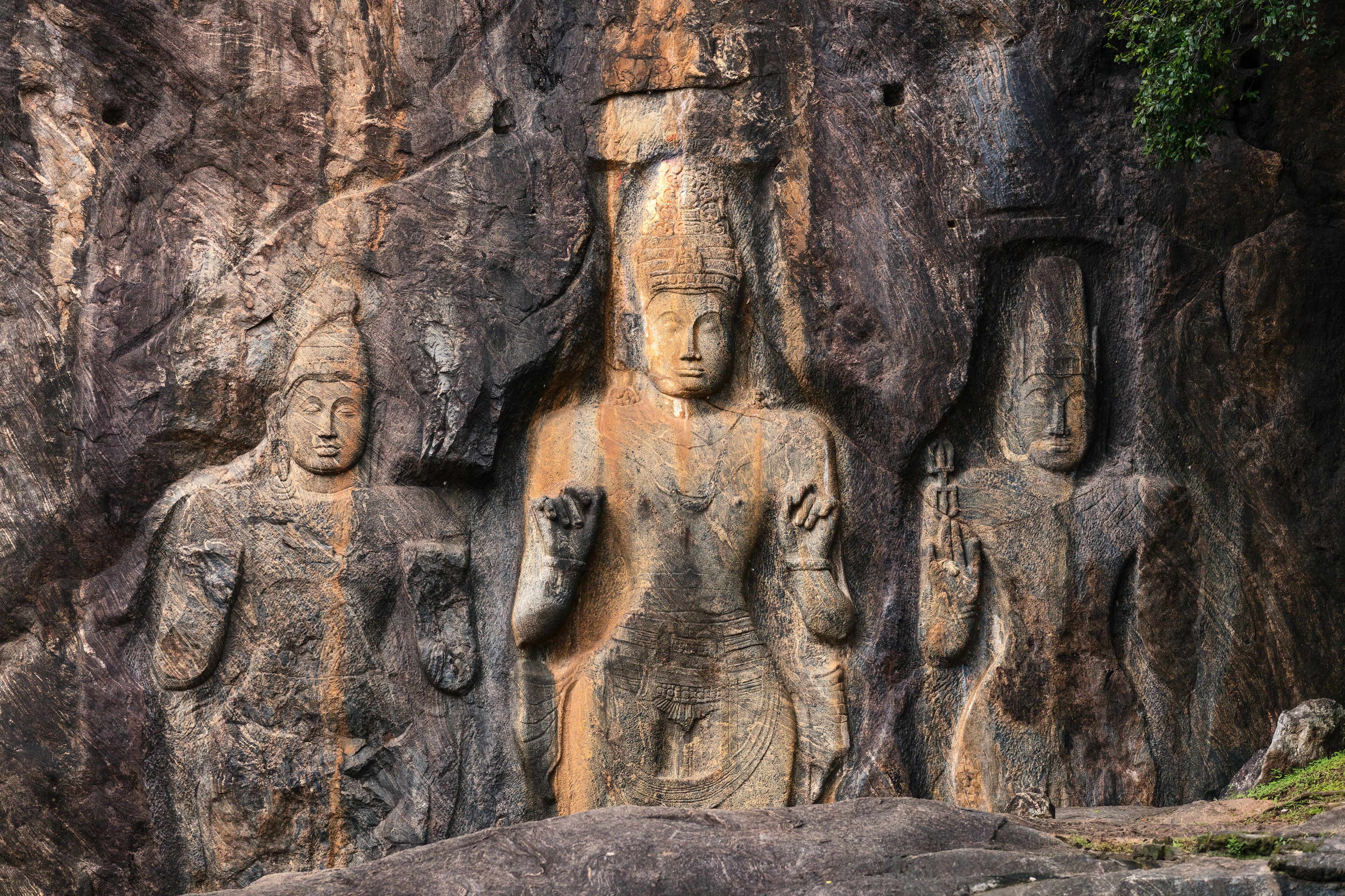 A large rock face with three carved statues of standing figures.