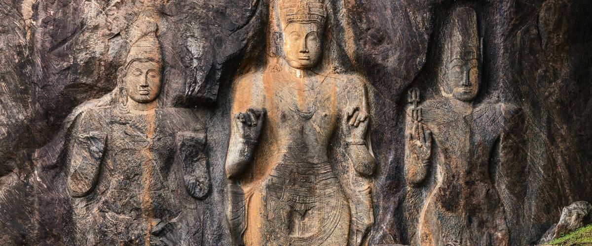 A large rock face with three carved statues of standing figures.