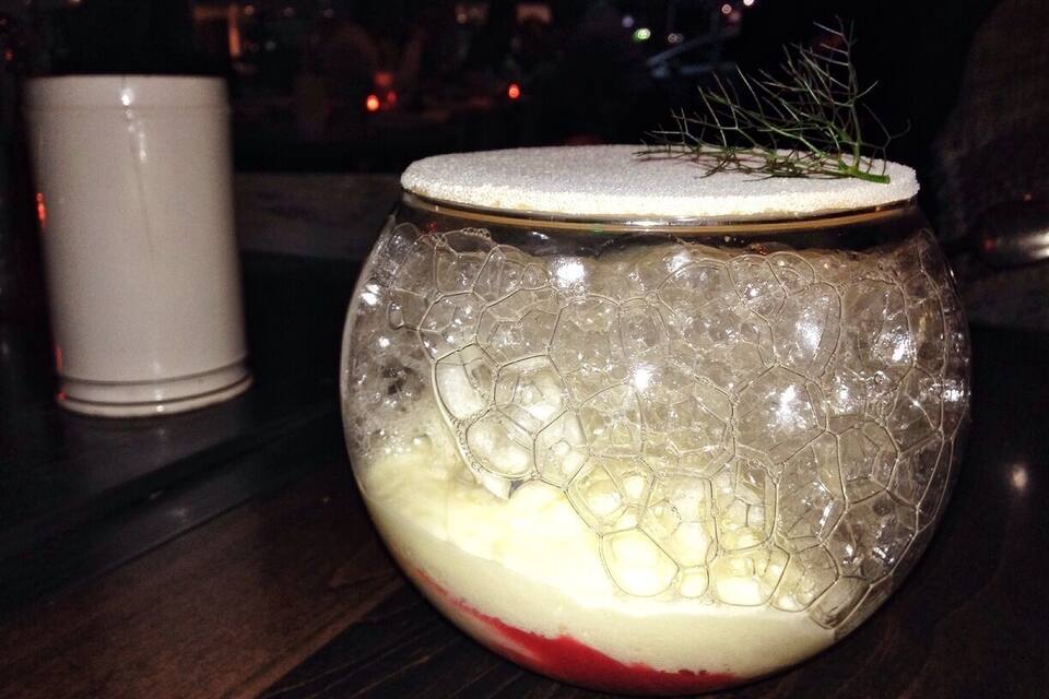 A glass bowl with a textured pattern and a white lid, containing a red substance and a sprig of greenery.