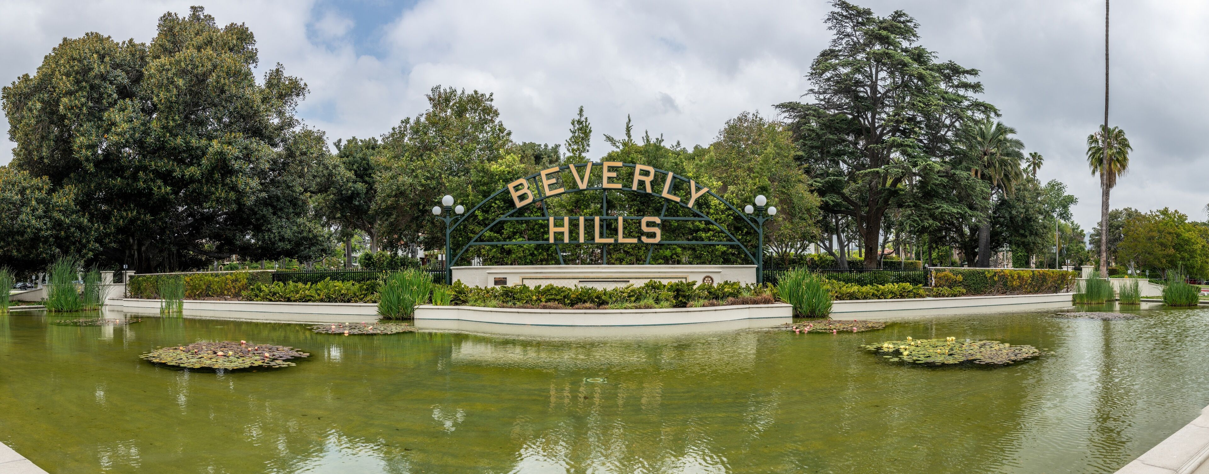 A sign reading "BEVERLY HILLS" surrounded by a pond with lily pads and a well-maintained garden.