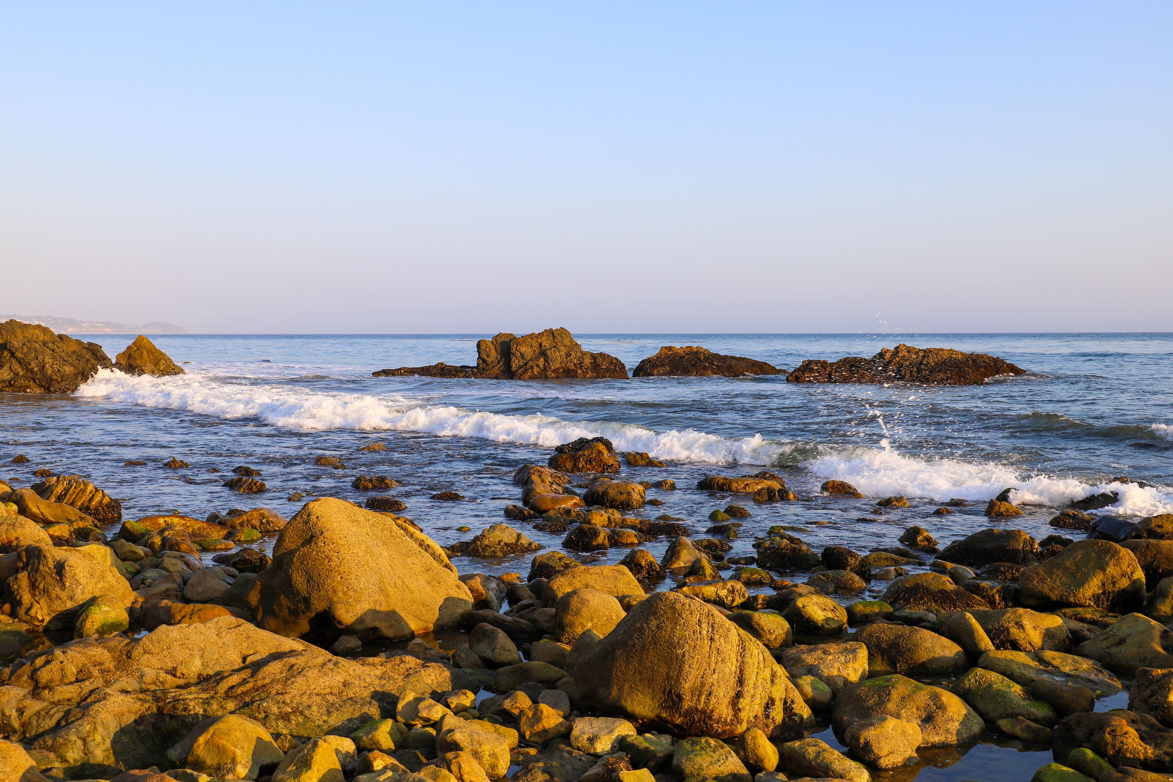 A rocky shoreline with waves crashing against the rocks and the ocean in the background.