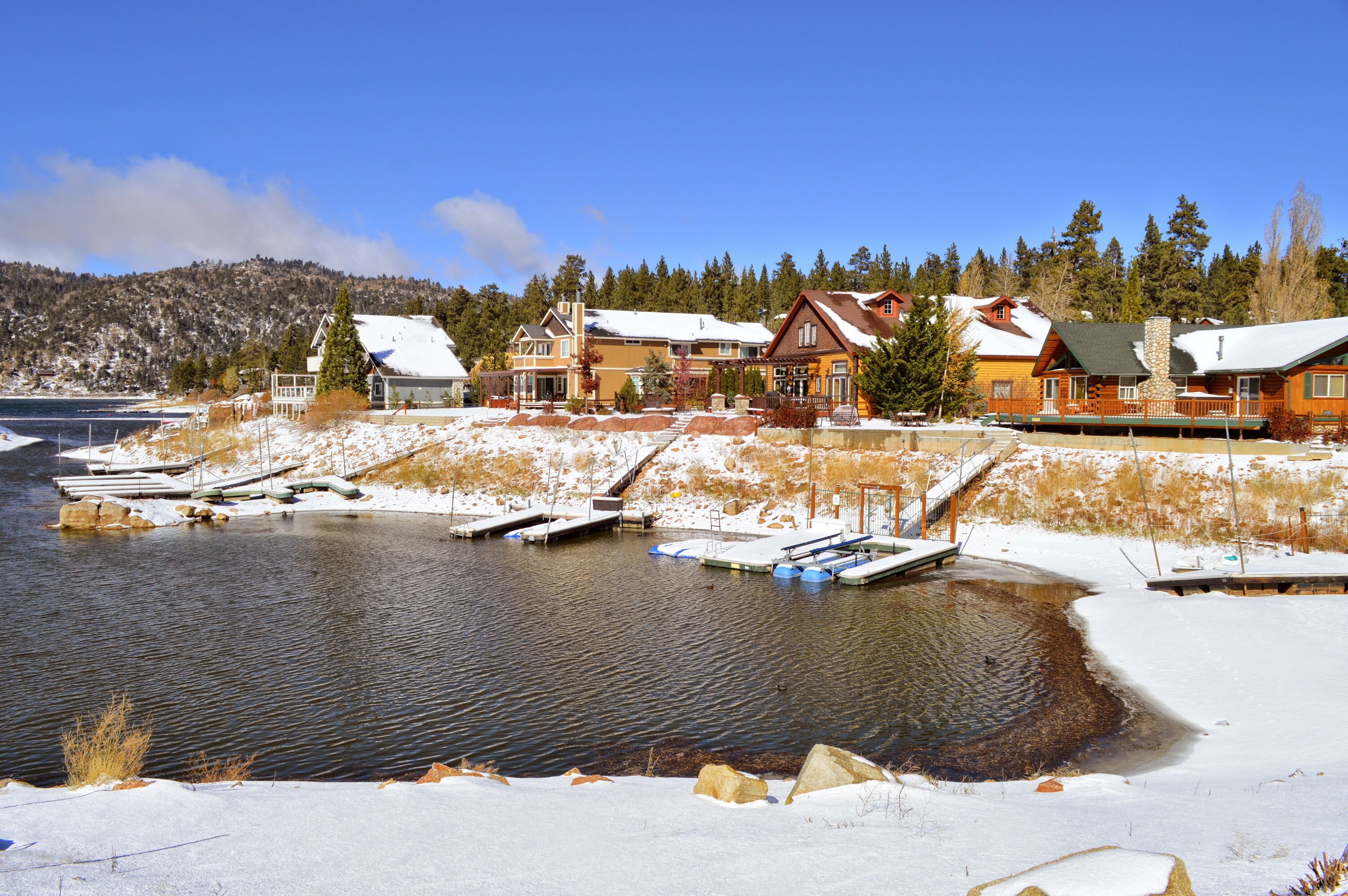 A lakeside cabin community with snow-covered ground, docked boats, and surrounding trees.
