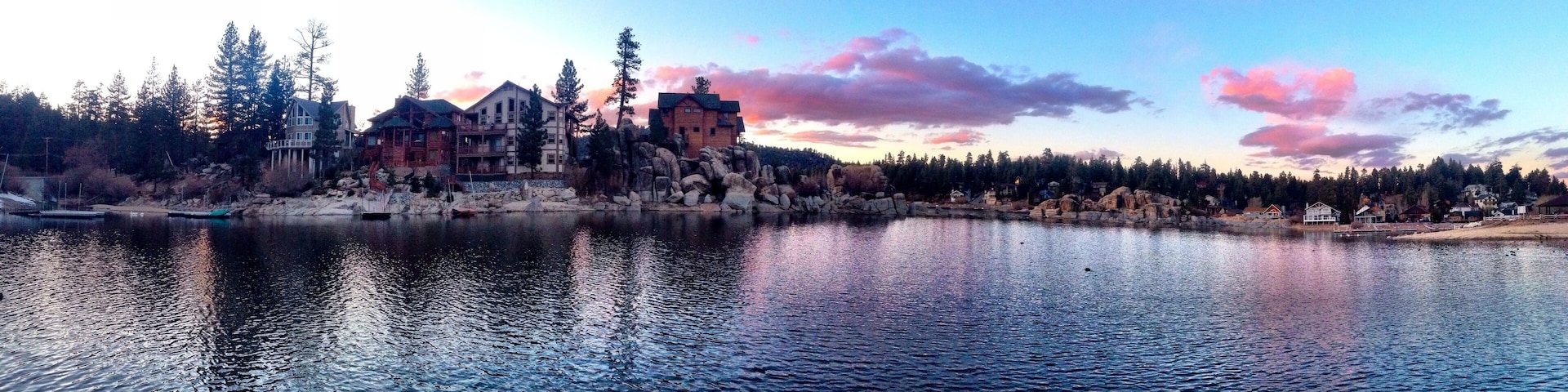 A lakeside view with a large wooden house and several smaller buildings, surrounded by trees and rocks.