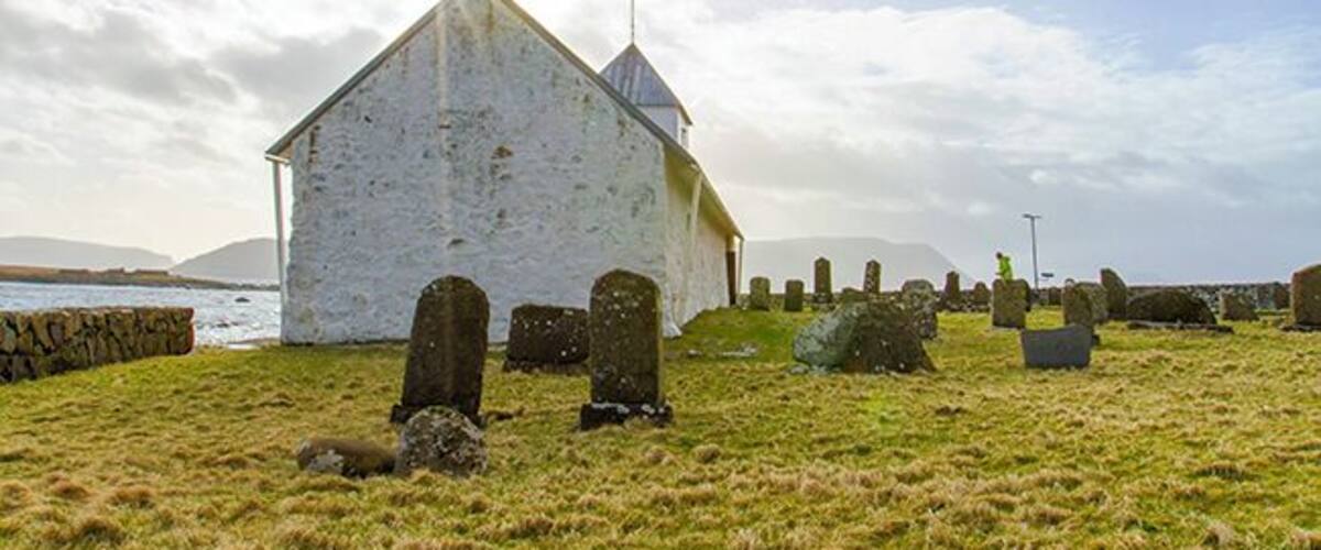 A white church with a steeple, surrounded by gravestones and a grassy field.