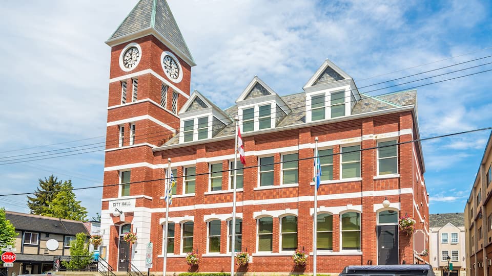A historic brick building with a clock tower, a red car, and a black SUV parked in front.