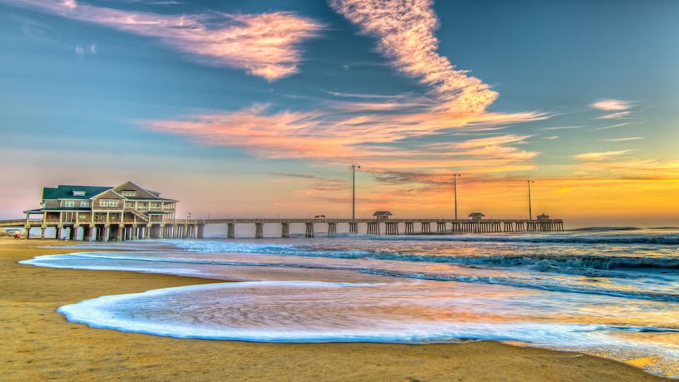A beach with waves, a pier, and a house.