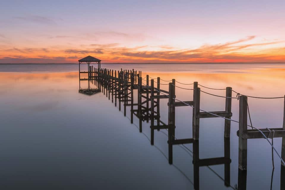 A wooden pier extending into calm waters at sunset.