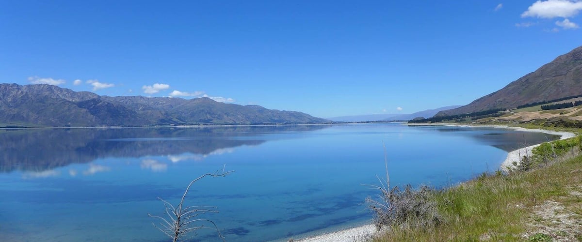Un lago tranquilo rodeado de montañas bajo un cielo azul despejado.