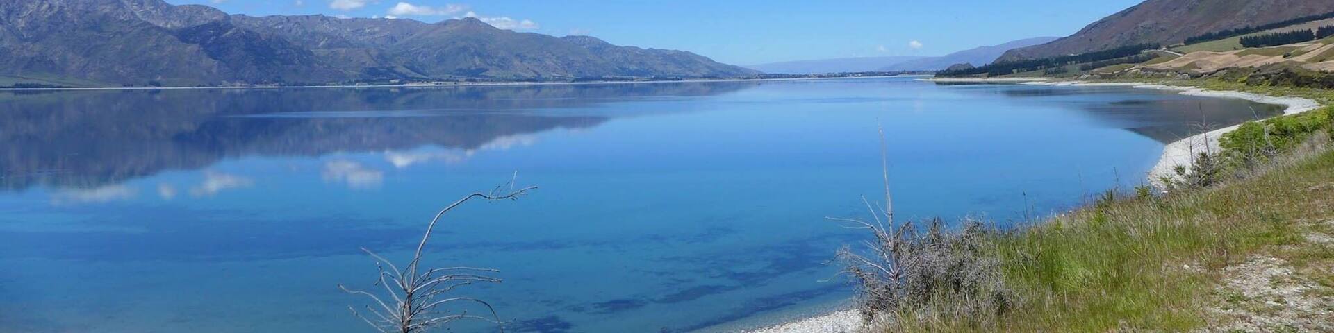 A calm lake surrounded by mountains under a clear blue sky.