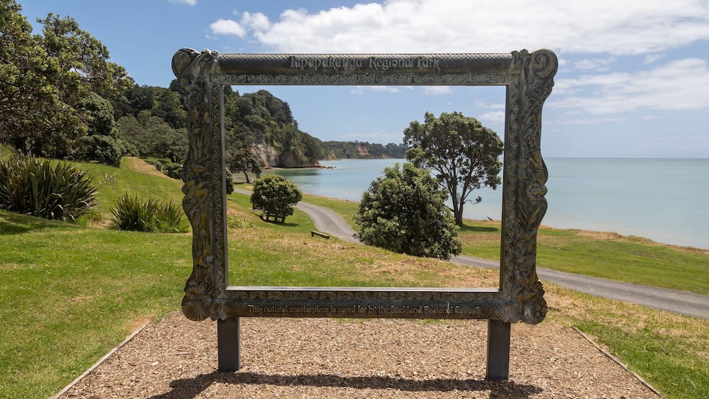 A scenic view through a decorative frame at Lavapekanga Regional Park, overlooking a coastal landscape with trees and a clear sky.
