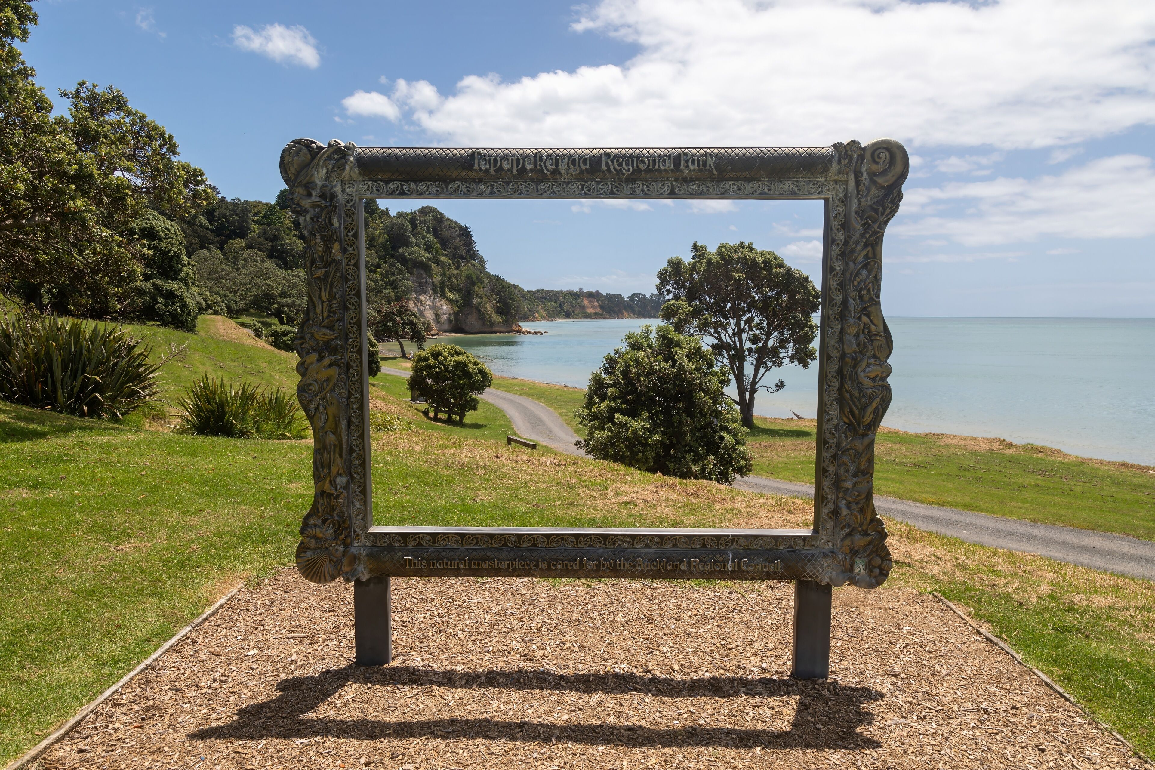 A scenic view through a decorative frame at Lavapekanga Regional Park, overlooking a coastal landscape with trees and a clear sky.