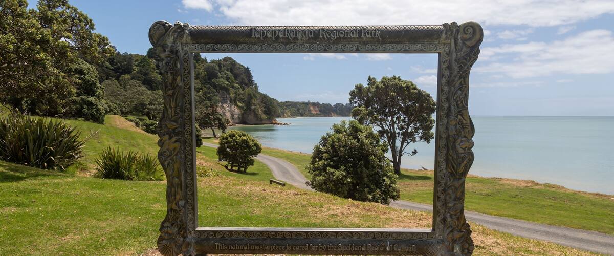 A scenic view through a decorative frame at Lavapekanga Regional Park, overlooking a coastal landscape with trees and a clear sky.