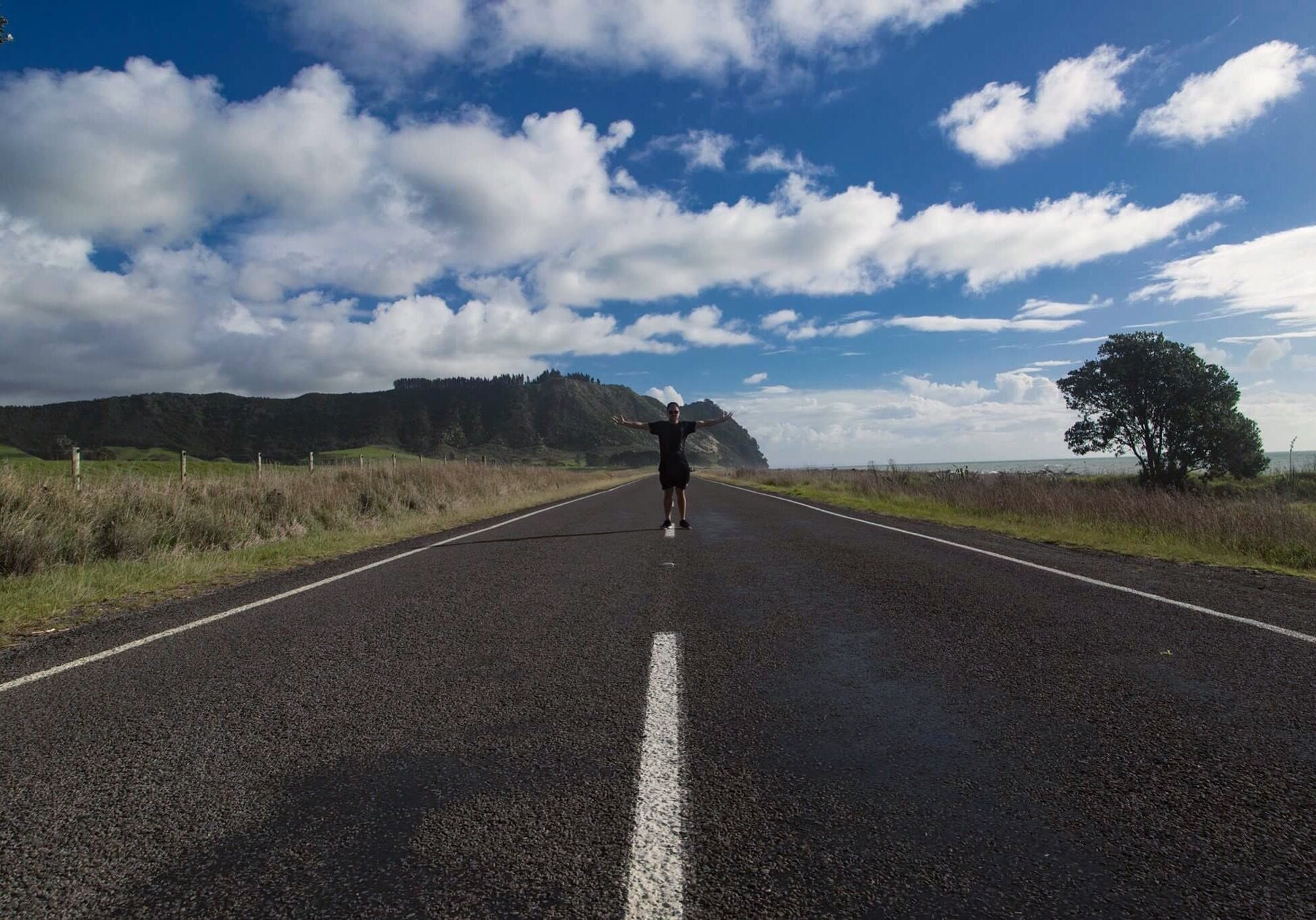A road with a person standing in the center, surrounded by a clear sky and distant mountains.