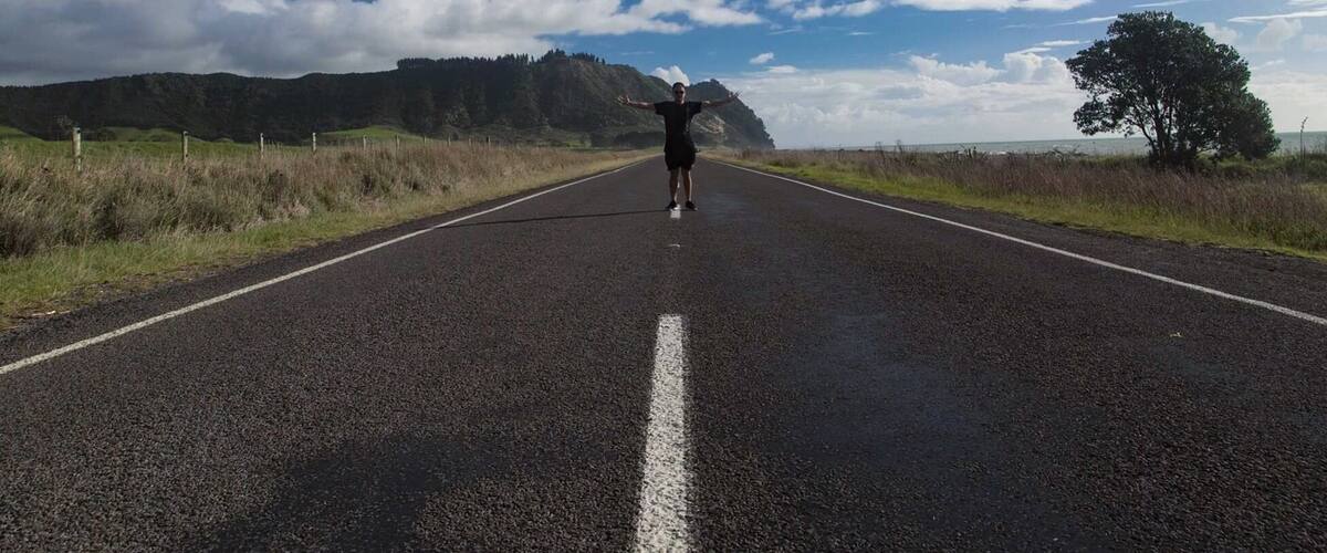A road with a person standing in the center, surrounded by a clear sky and distant mountains.