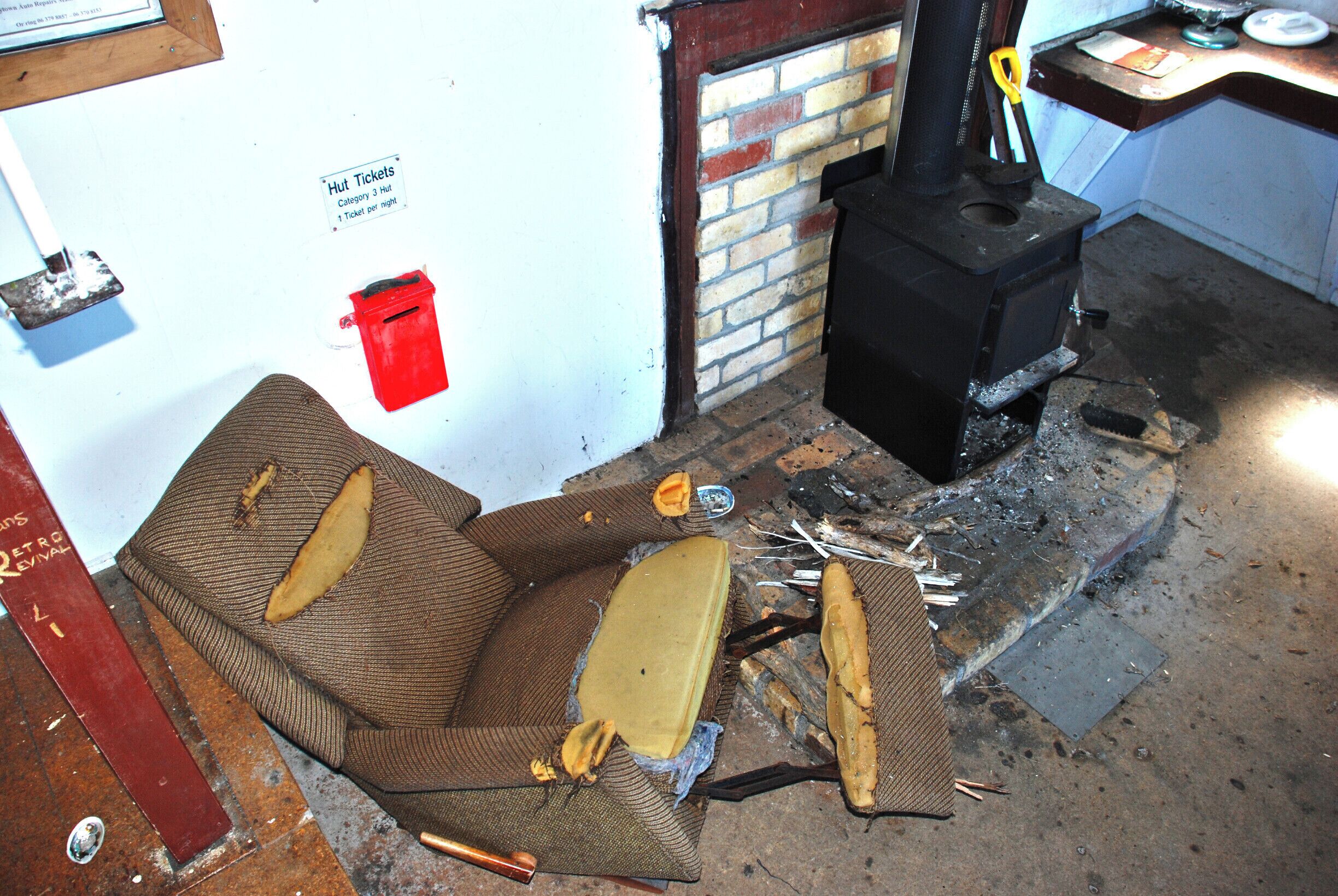 A damaged sofa, a red mailbox, and a black stove in a room with a brick wall and a door.