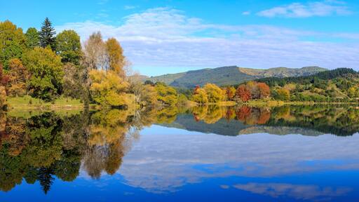 A calm lake reflecting trees and mountains.
