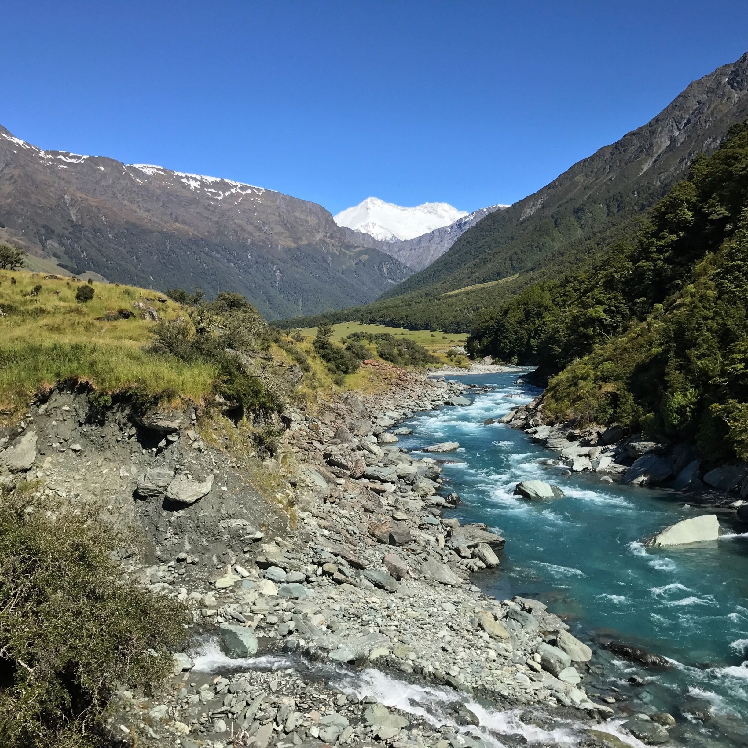A river flowing through a mountainous valley with rocky terrain and snow-capped peaks in the background.