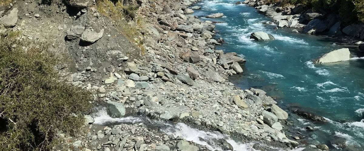 A river flowing through a mountainous valley with rocky terrain and snow-capped peaks in the background.