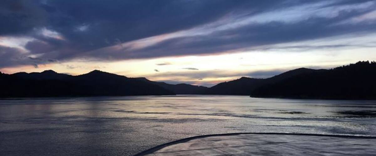 A calm lake at sunset with mountains in the background.