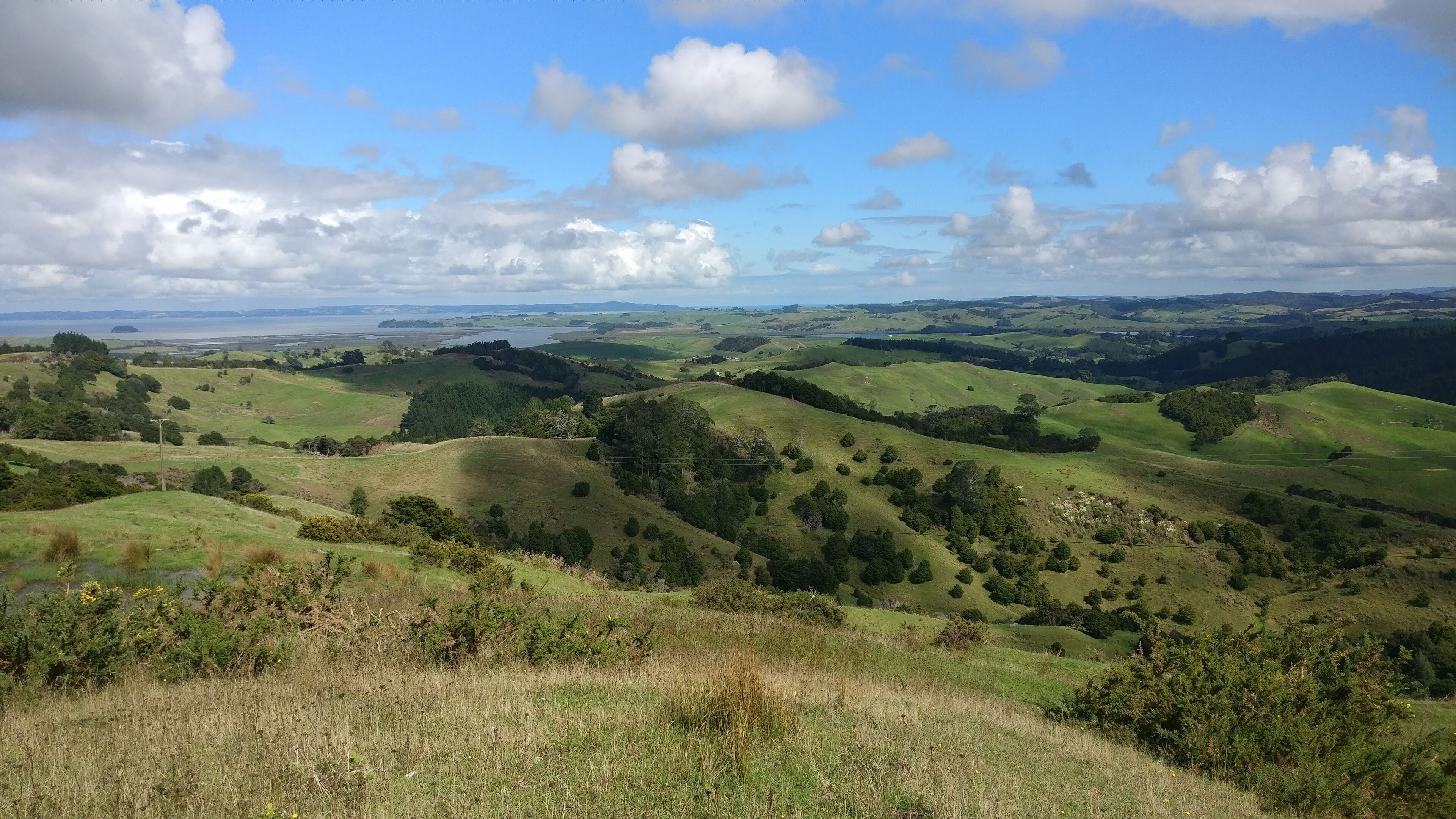 Rolling green hills, a distant body of water, and a clear sky with clouds.