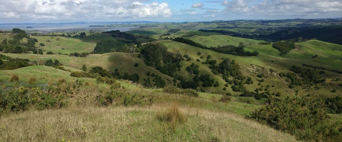 Rolling green hills, a distant body of water, and a clear sky with clouds.