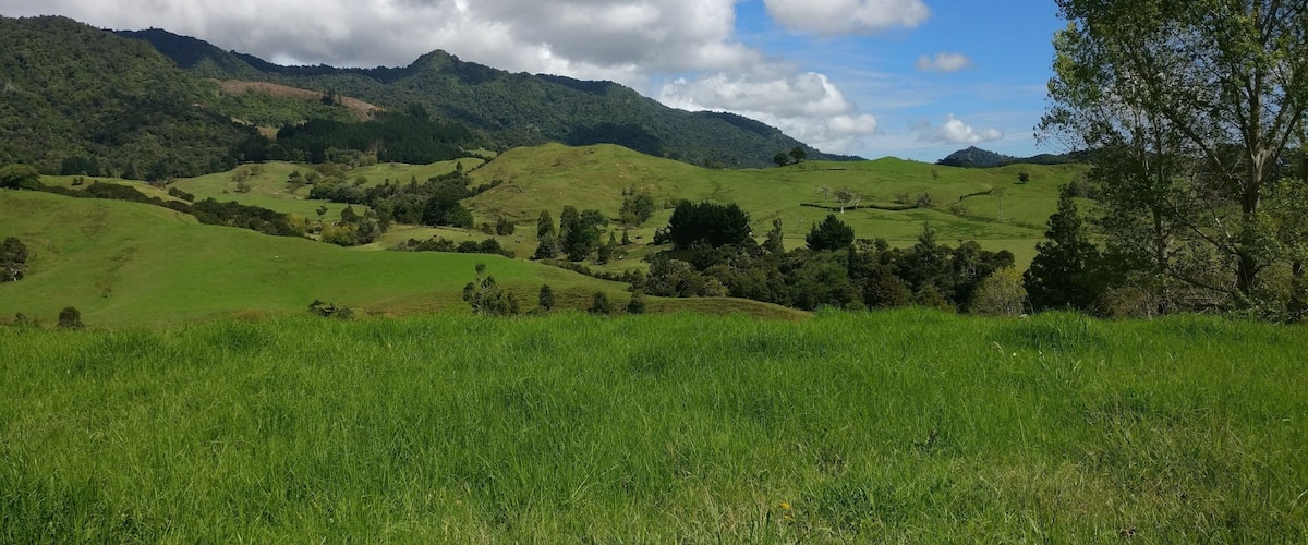 Rolling green hills, a clear sky with clouds, and a tree on the right.