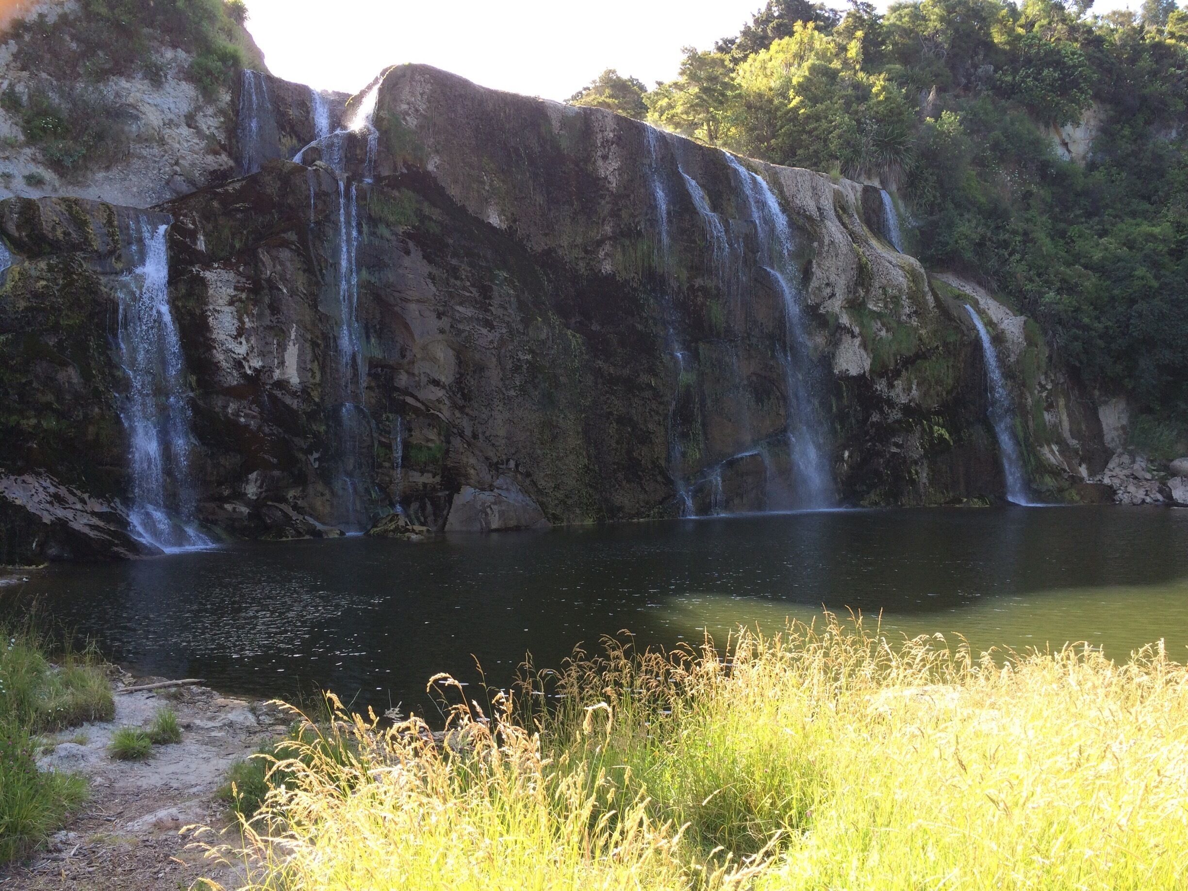 A waterfall cascading into a calm lake surrounded by rocky cliffs and lush greenery.