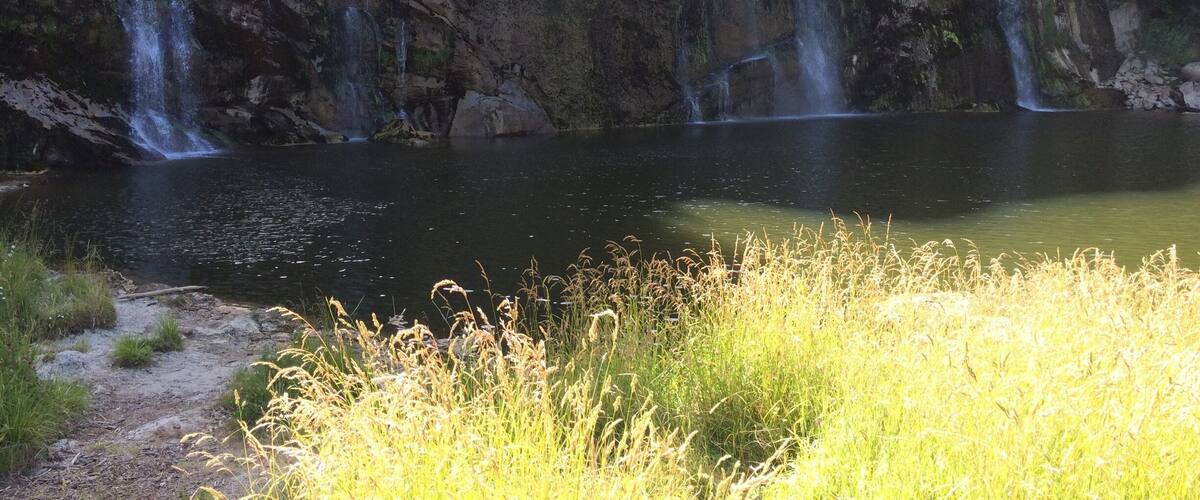 A waterfall cascading into a calm lake surrounded by rocky cliffs and lush greenery.