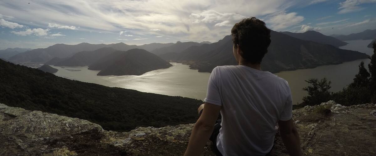 A person sitting on a rocky outcrop overlooking a lake surrounded by mountains.