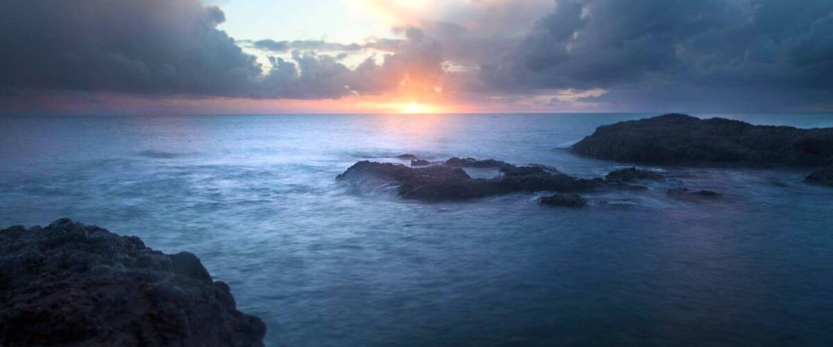 A sunset over a rocky coastline with calm sea and clouds.
