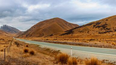 Camí a través d'un paisatge sec i amb turons, amb muntanyes al fons.