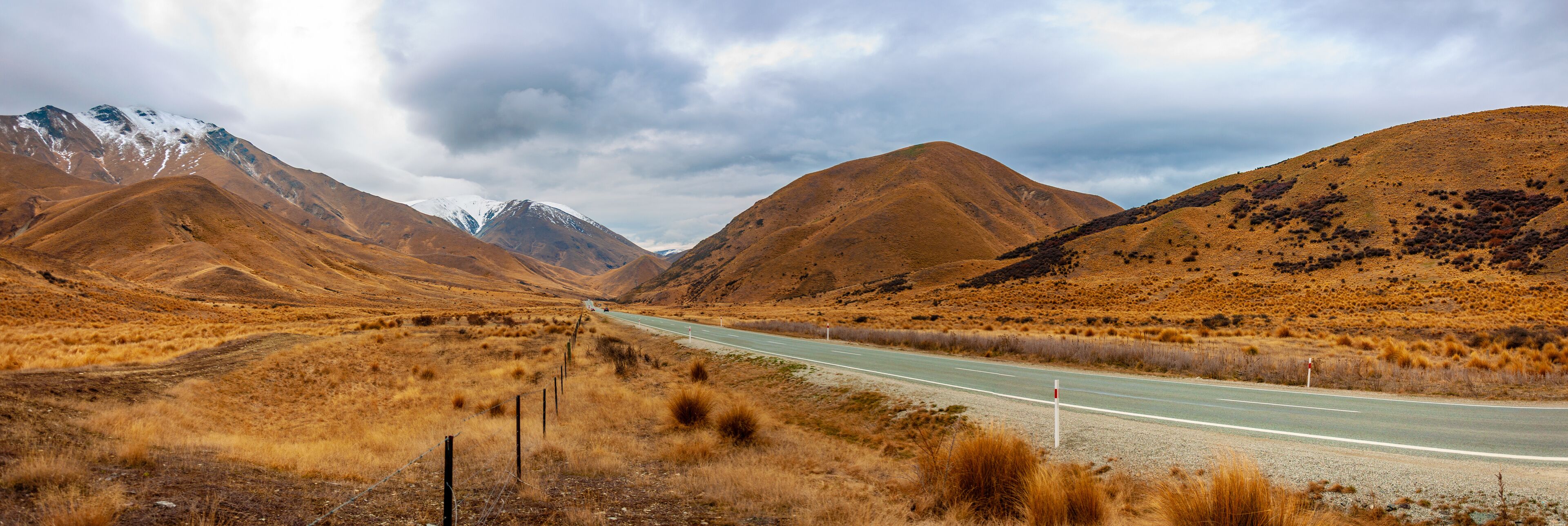 A road through a dry, hilly landscape with mountains in the background.