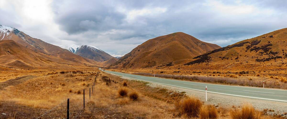 A road through a dry, hilly landscape with mountains in the background.