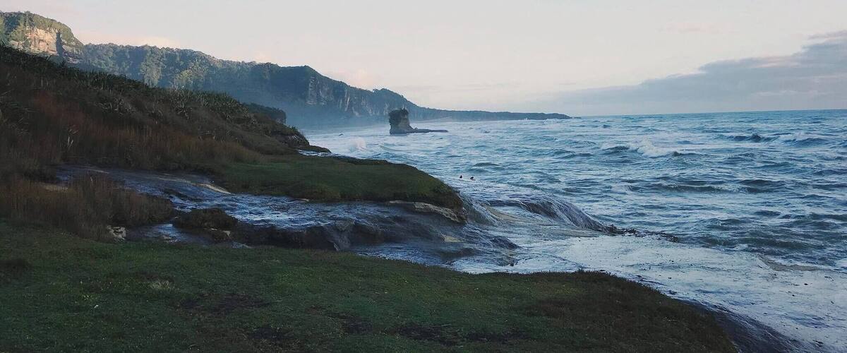 A coastal landscape with cliffs, a rocky outcrop, and a river.
