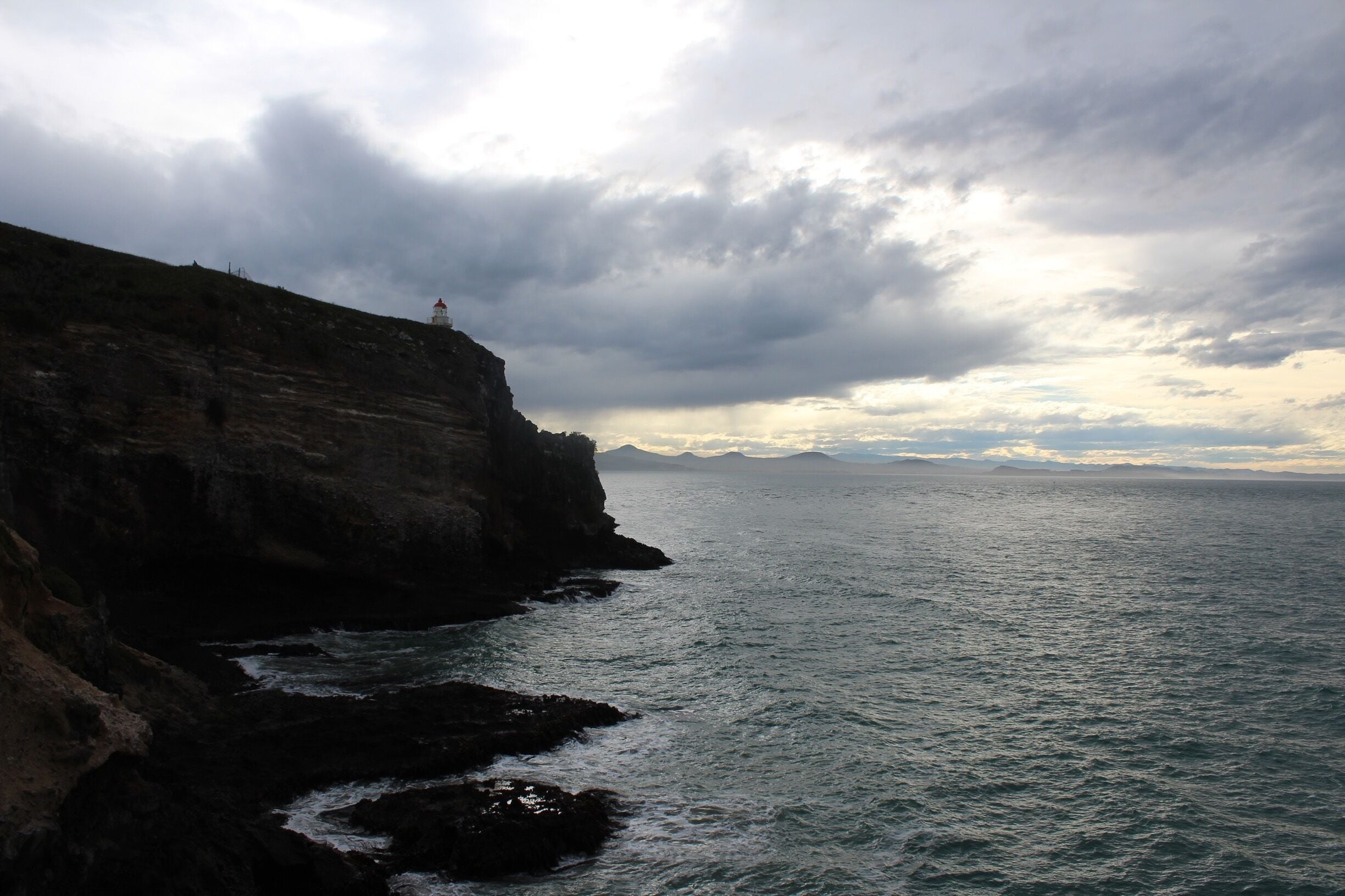 Acantilado costero con un faro, costa rocosa y cielo nublado.