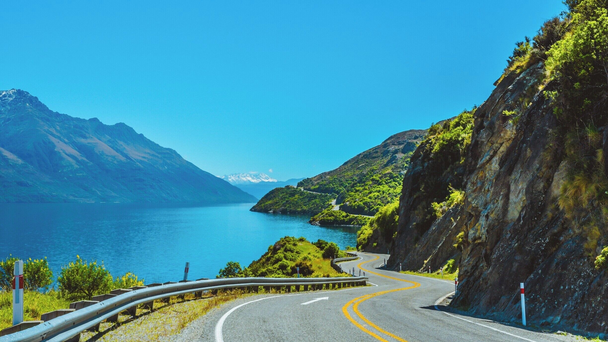 A winding mountain road with a view of a lake and mountains.