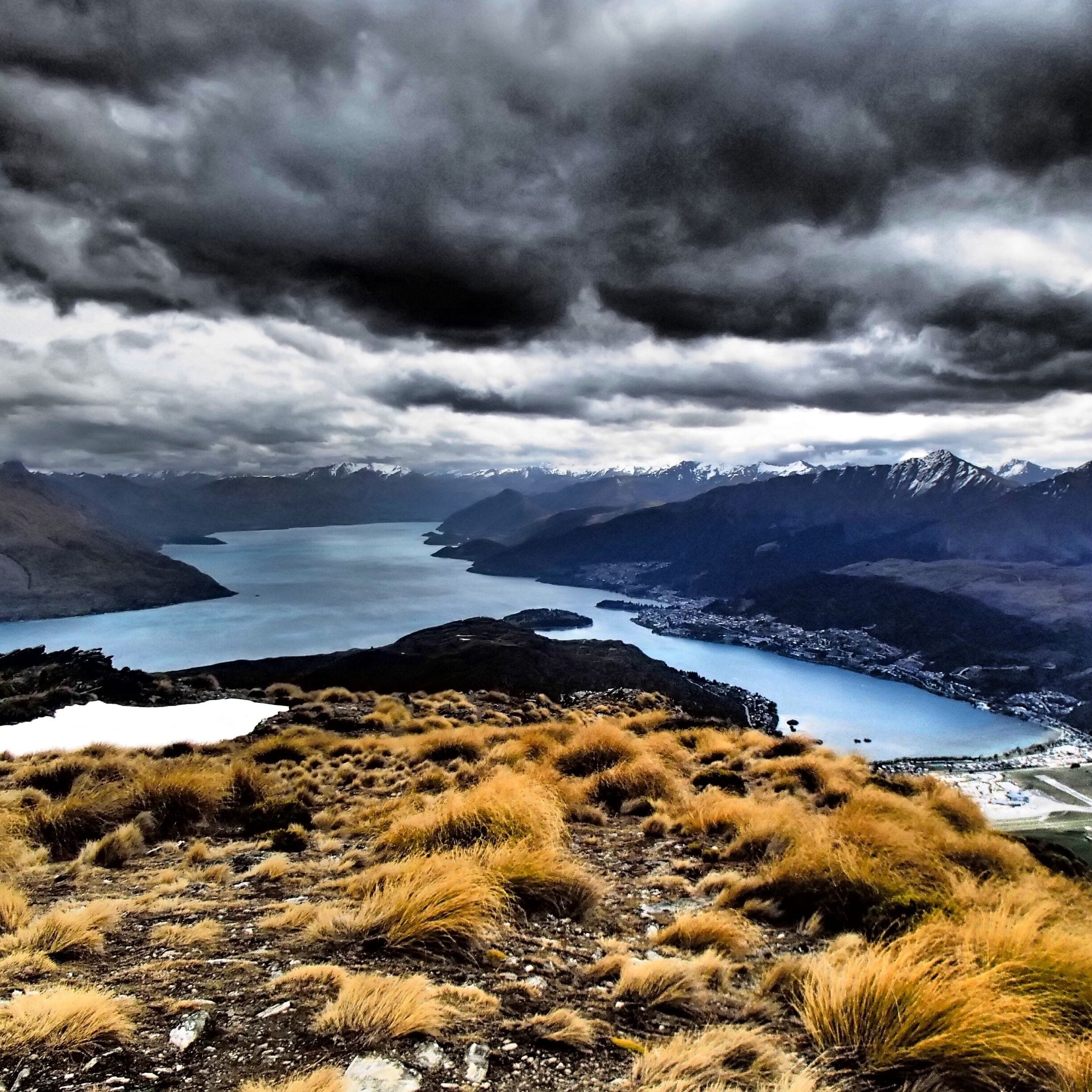 Paisagem montanhosa com um lago, picos nevados e uma cidade no vale.