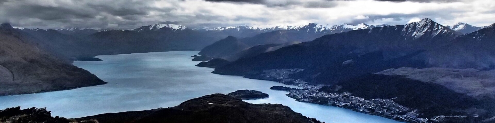 Paisagem montanhosa com um lago, picos nevados e uma cidade no vale.