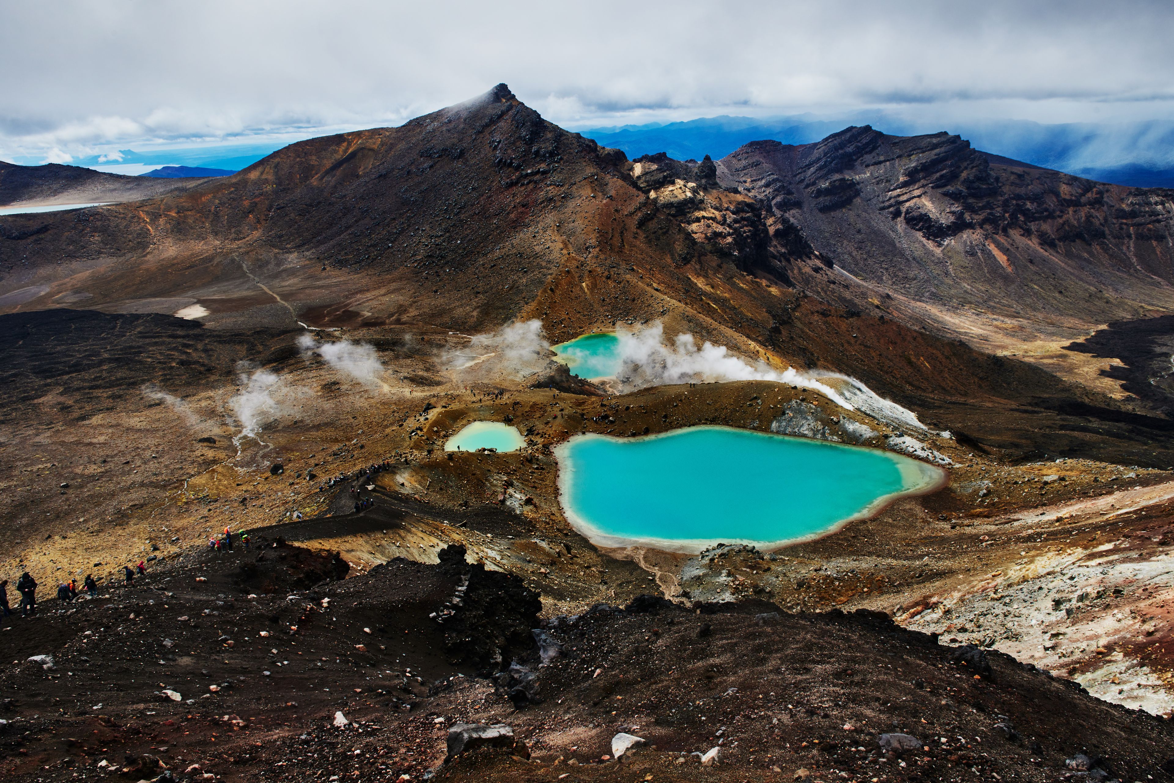 Un paysage montagneux caractérisé par des phénomènes géothermiques, notamment des sources chaudes aux eaux turquoise et des évents de vapeur.