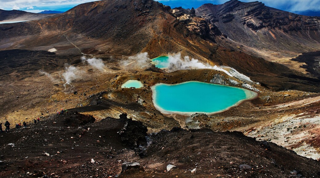 Un paysage montagneux caractérisé par des phénomènes géothermiques, notamment des sources chaudes aux eaux turquoise et des évents de vapeur.
