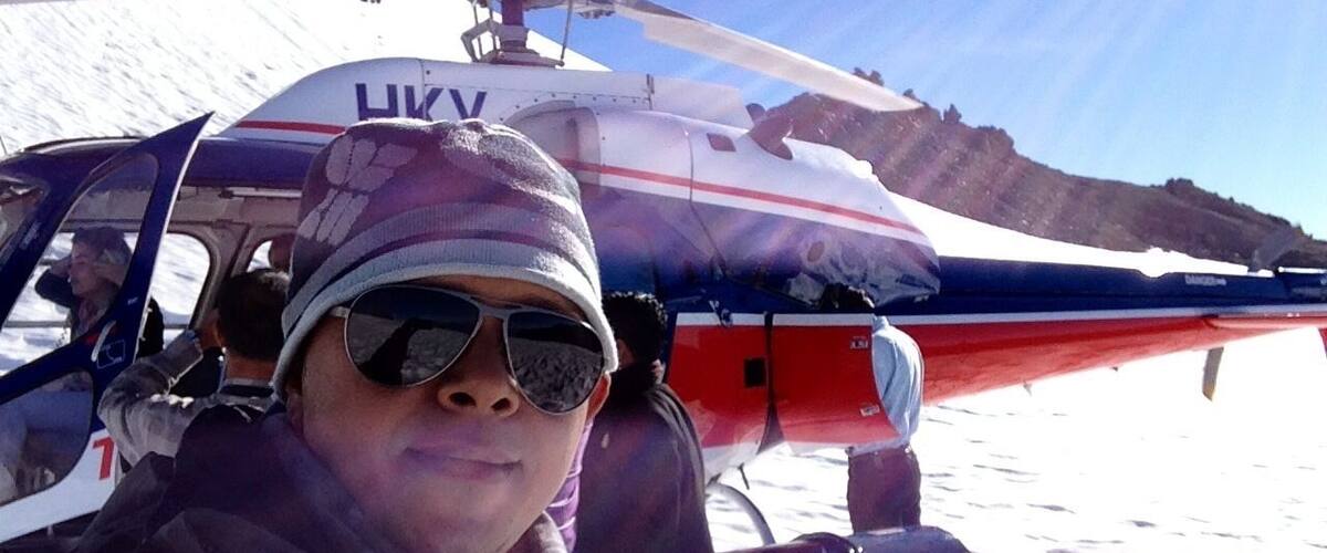 A helicopter with "HKV" and "TOPTER" written on it, parked on snow-covered ground with mountains in the background.