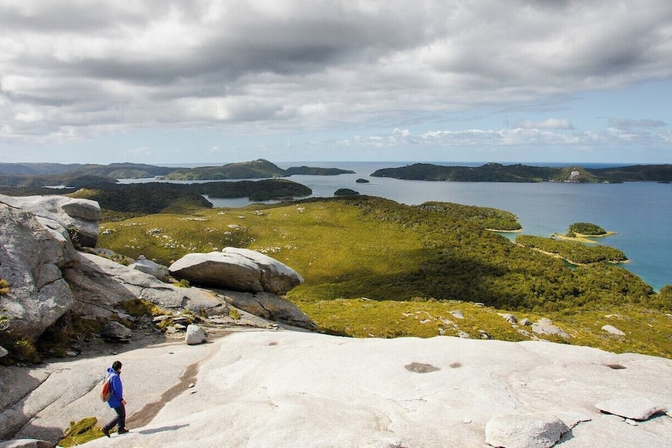 A hiker on a rocky path overlooking a coastal landscape with islands and a large body of water.