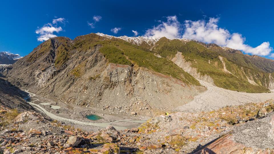 A mountainous landscape with a glacier, rocky terrain, and a clear blue sky.