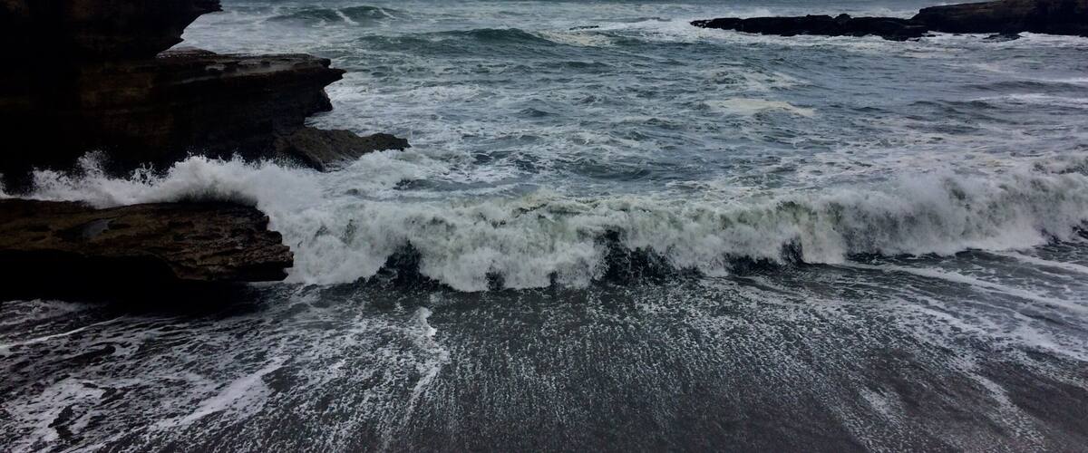 A rocky coastline with waves crashing against the shore under a cloudy sky.