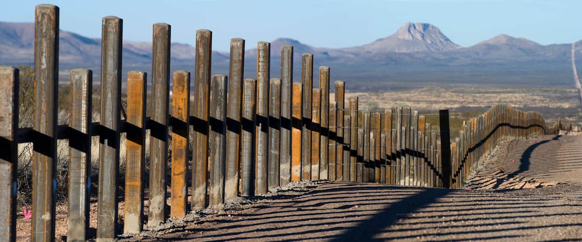 A rusted metal fence with a mountain in the background.