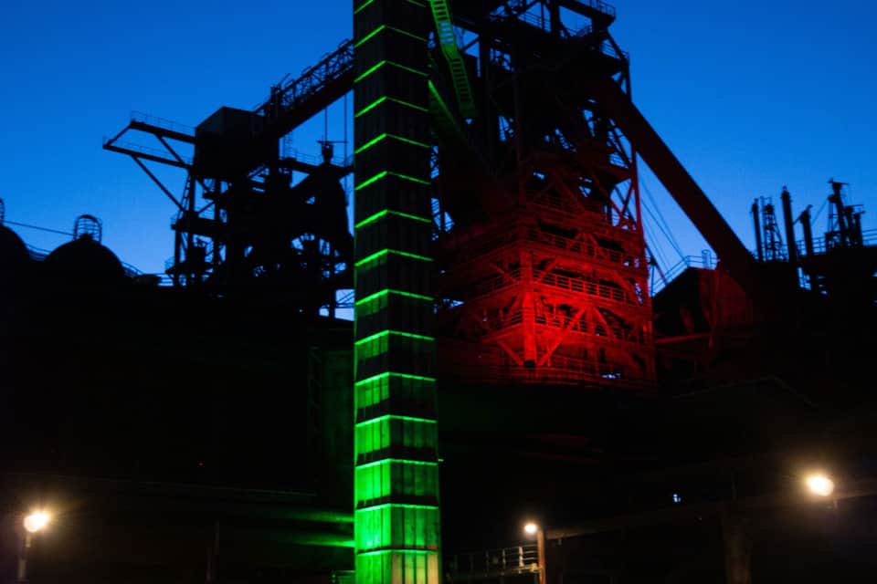 A large industrial structure with green and red lighting at dusk.