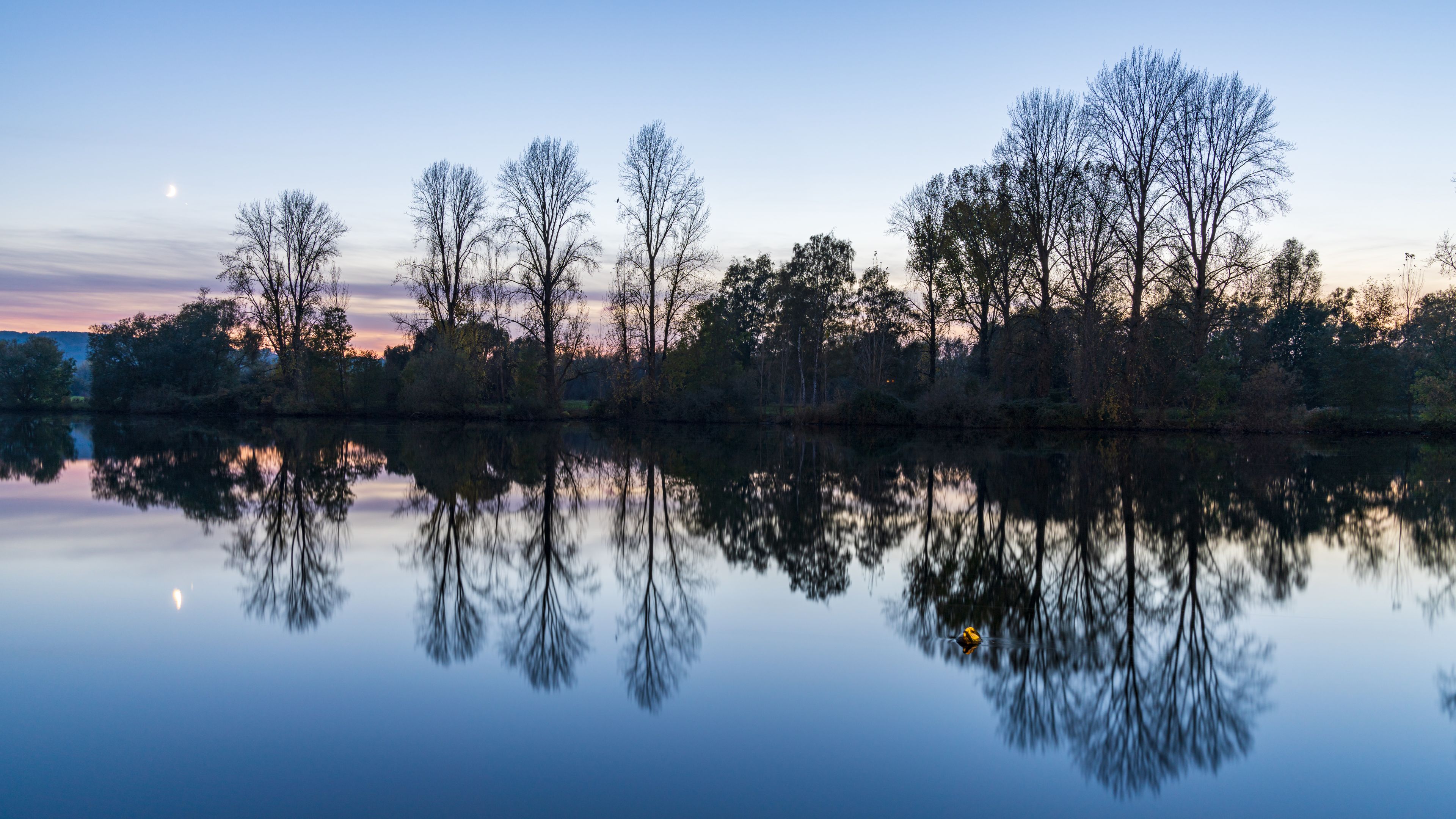 Un lac paisible où se reflètent les arbres et où le ciel est dégagé.