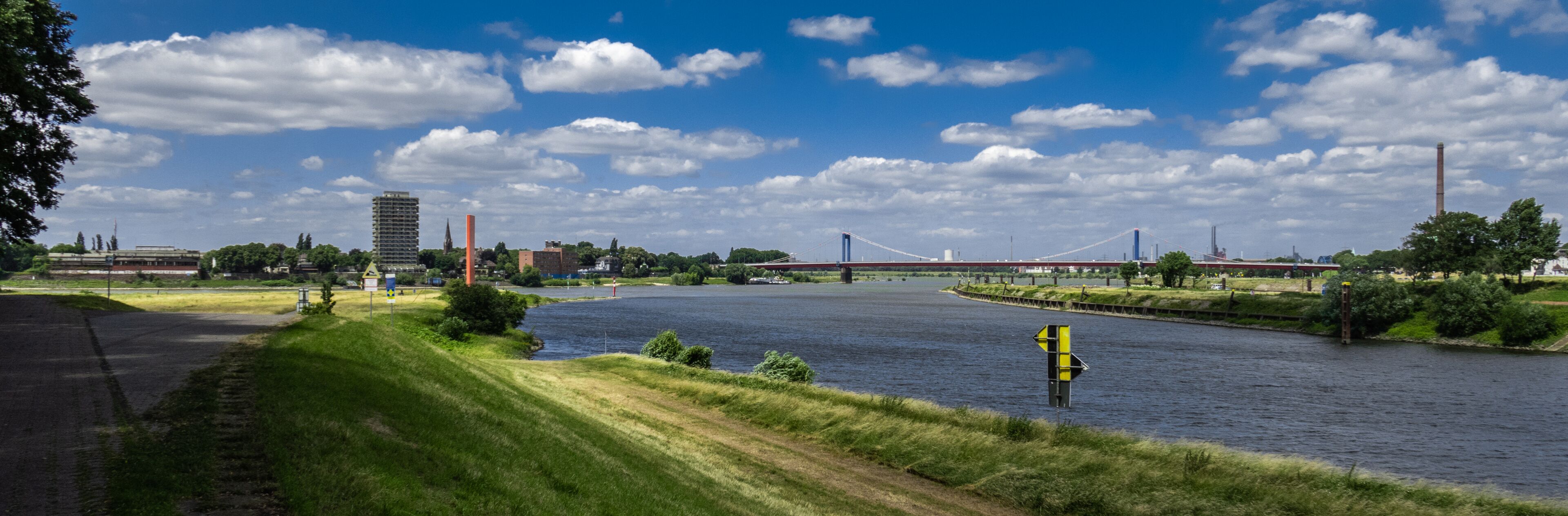 A river with a bridge, a tall building, and a red tower in the background.