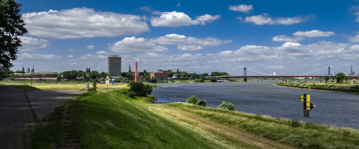 A river with a bridge, a tall building, and a red tower in the background.